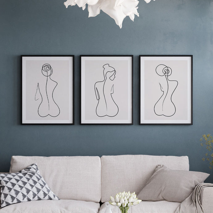 A set of 3 nude woman line art prints framed above a sofa